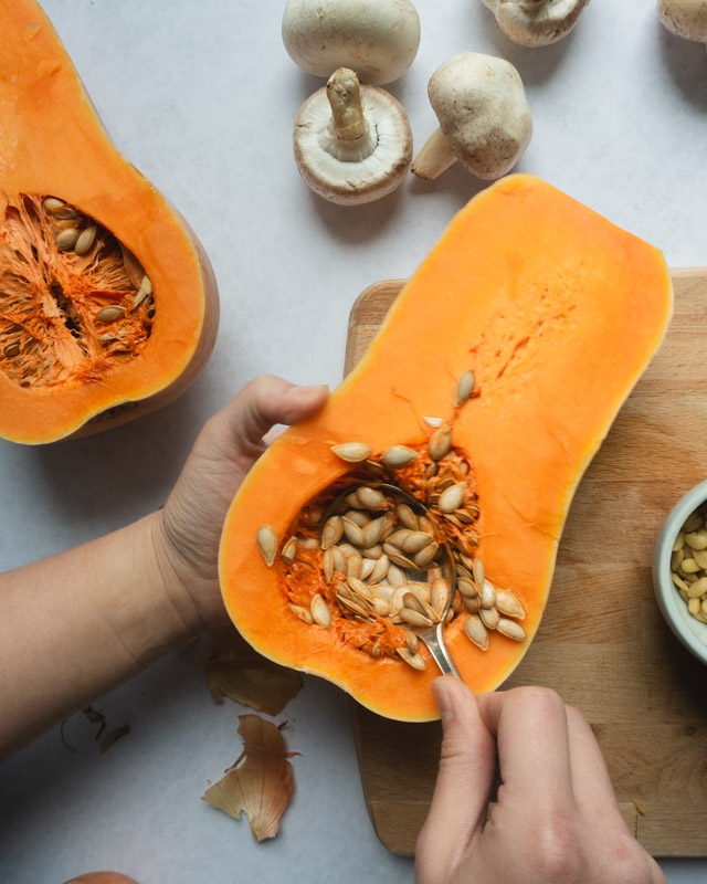 scooping out seeds of halved butternut squash