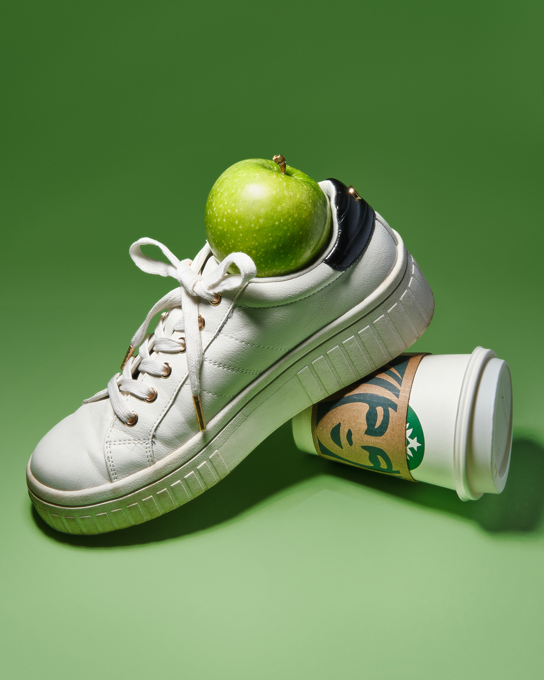 white trainer shoe with a green apple inside, propped up on a starbucks cup
