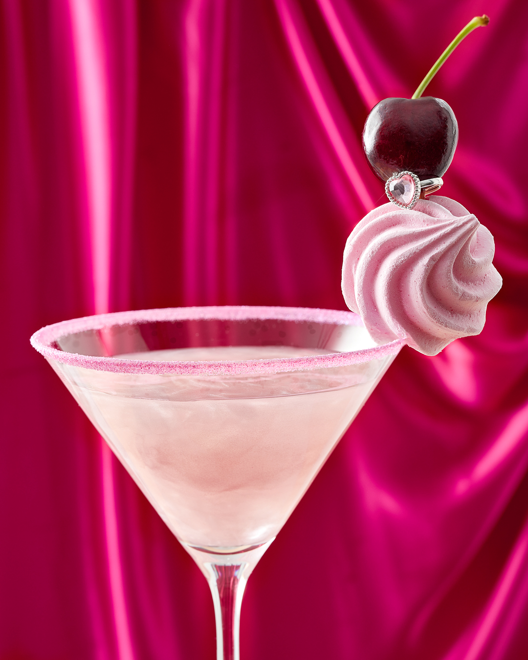 martini glass with pale pink cocktail and sparkly rim, garnished with a pink meringue swirl, sparkle ring and cherry